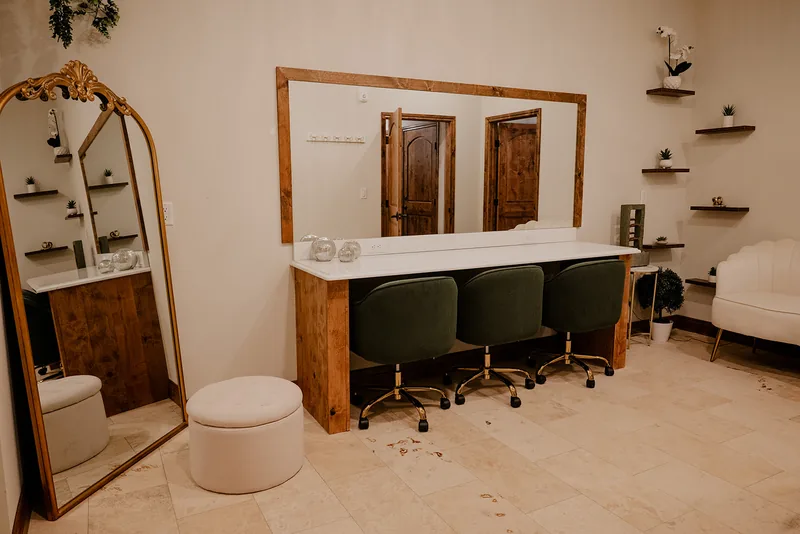 The bridal suite at The Arabella — a long wood-framed vanity mirror, three green velvet chairs, and a gold arched mirror beside a cream lounge chair