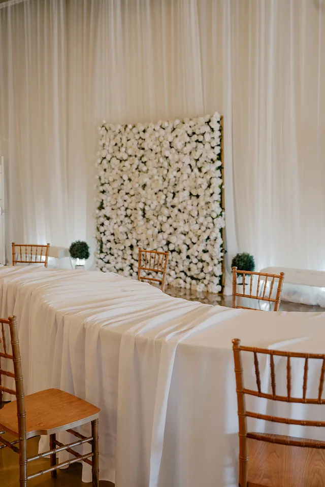 The white flower wall behind a draped head table